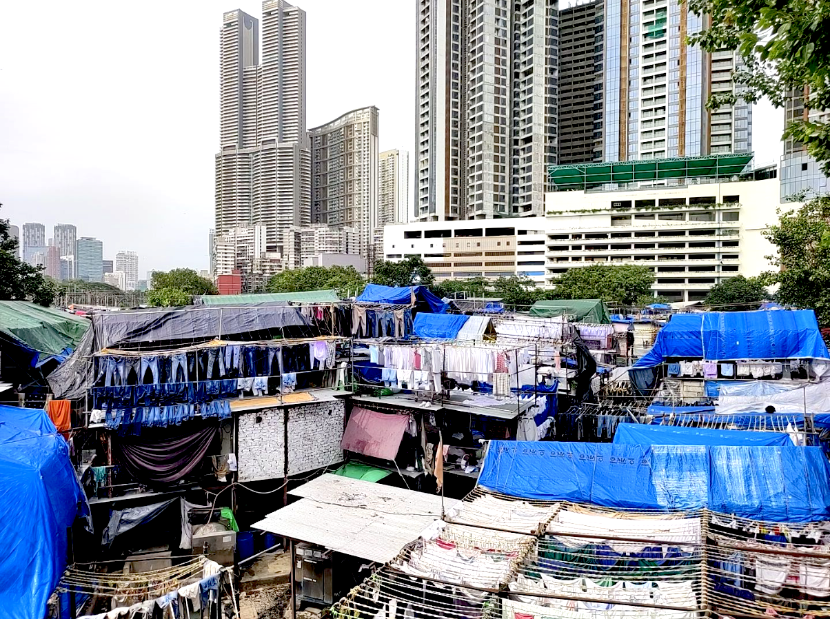 ムンバイの屋外洗濯場「ドービー・ガート（Mahalaxmi Dhobi Ghat）」。無数の物干しと青いシートの向こうに高層ビル群がそびえる風景