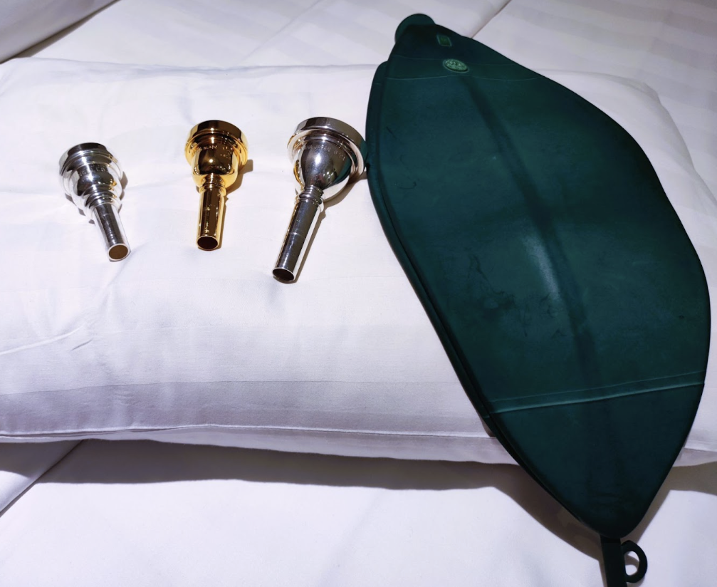 旅行に持参するトロンボーン用マウスピース3本とブレストレーニング用エアバッグを、ホテルの枕の上に並べた練習アイテム