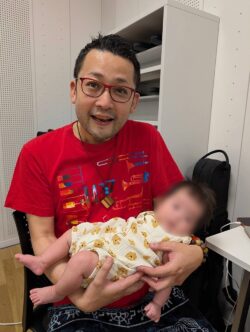 さいたま市（浦和・大宮・岩槻）で活動する社会人ジャズクラス「ALL AGE JAZZ PARADICE」の講師が、メンバーの赤ちゃんを抱く様子。音楽を通じて世代を超えた温かい交流が生まれていることを表す写真。